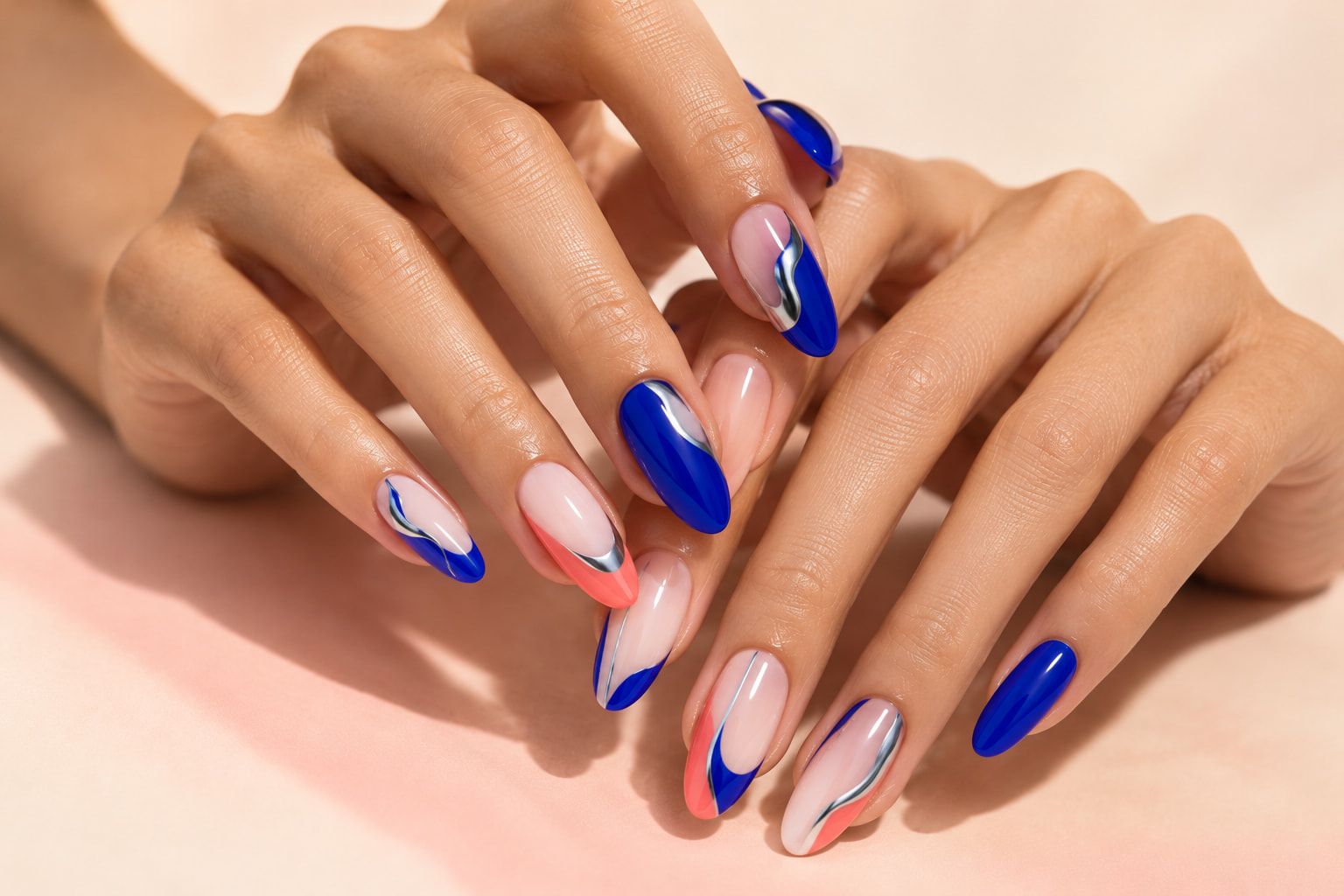 มือสองข้างกับเล็บทรงอัลมอนด์สีน้ำเงิน ปะการัง และนู้ด เพ้นท์ลายคลื่นขอบโครม